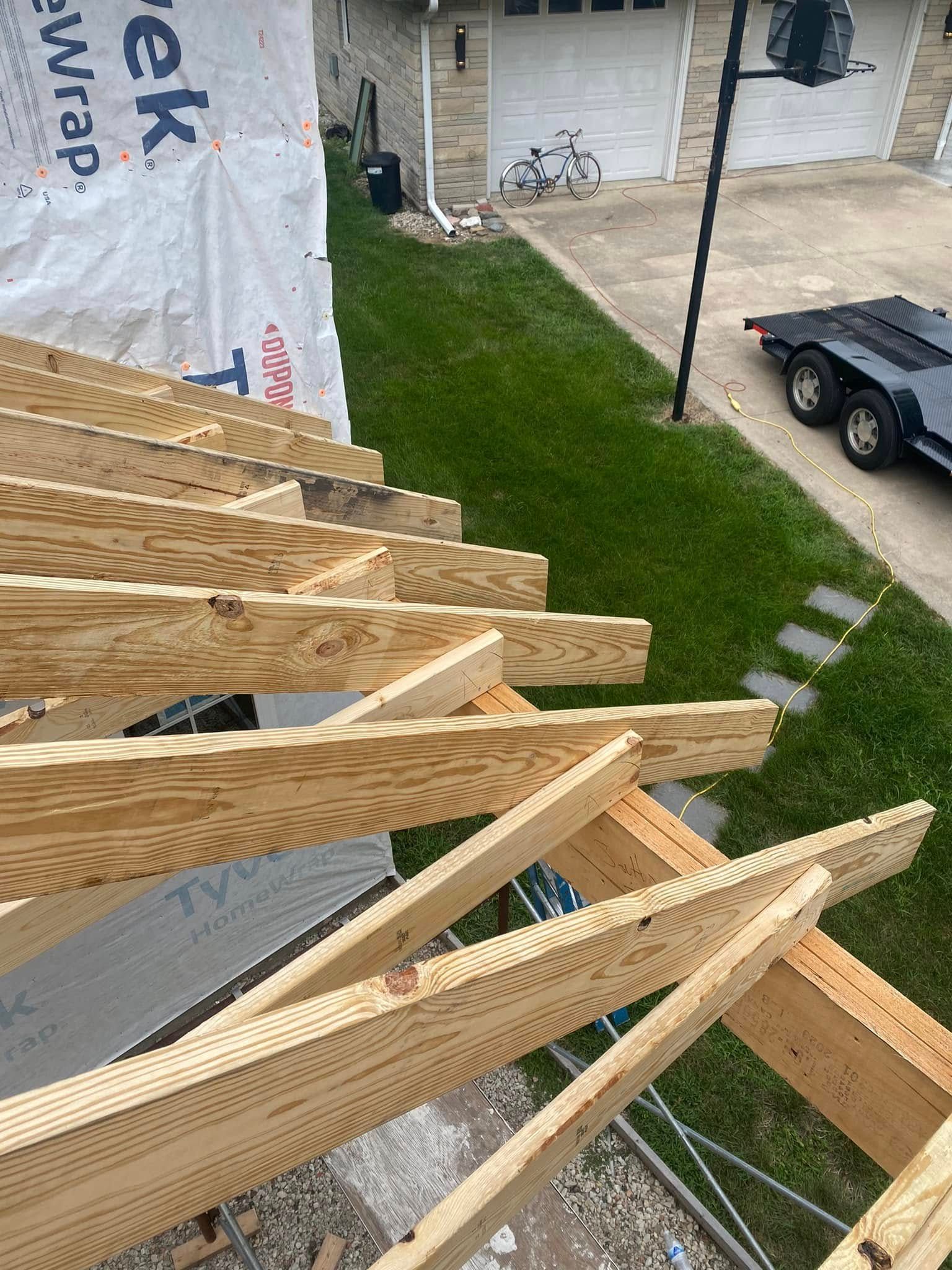 Wooden roof trusses under construction atop a house, with yard and parked truck below.