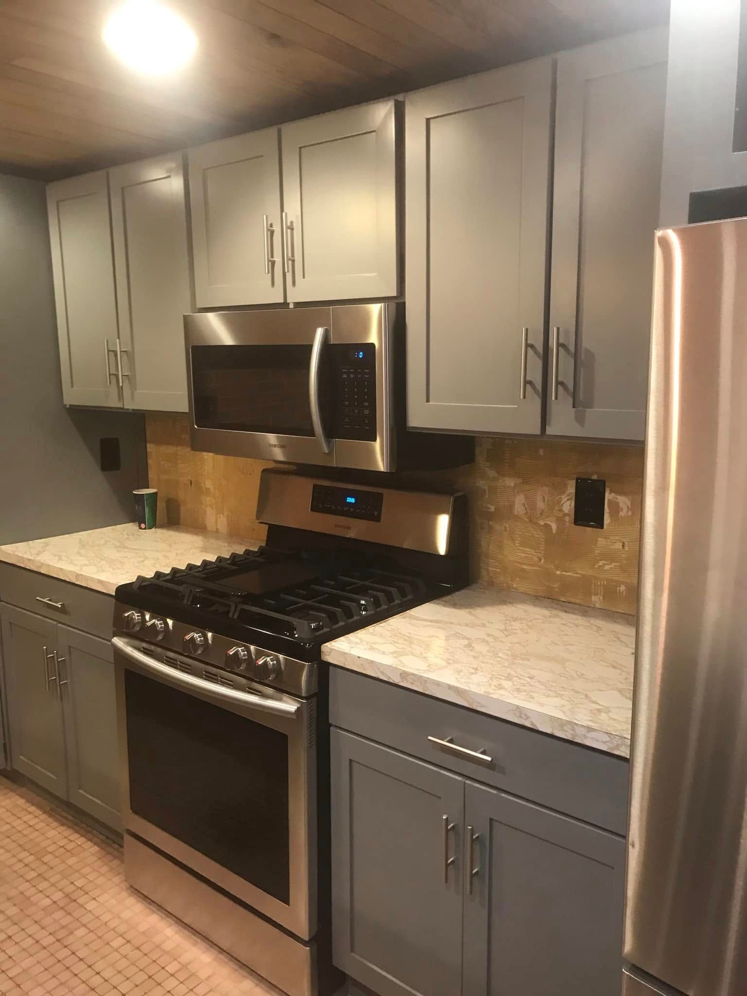 Modern kitchen with gray cabinets, stainless steel appliances, and light stone countertops