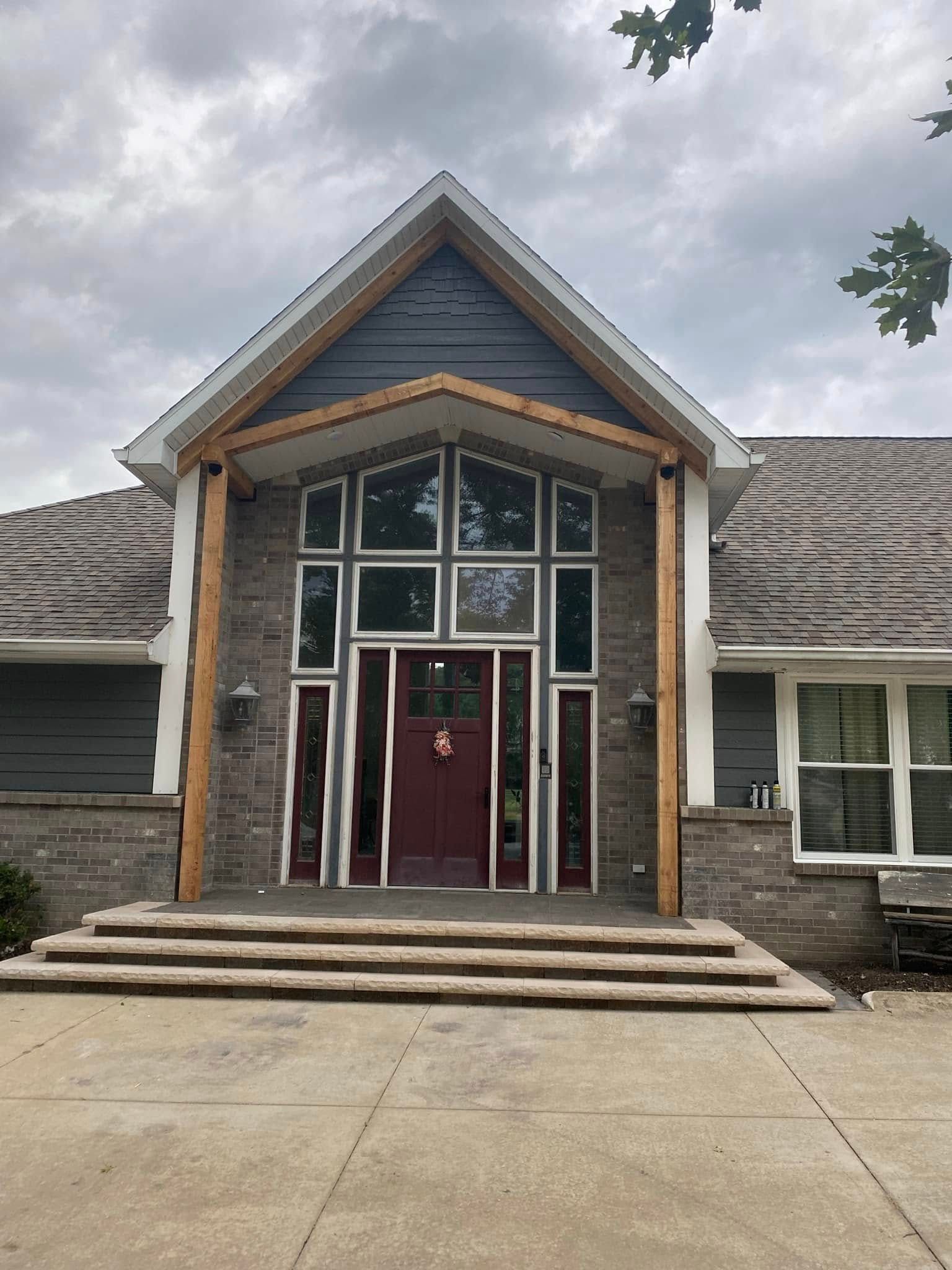 Front entrance of a stone building with a peaked roof, red door, and large windows.