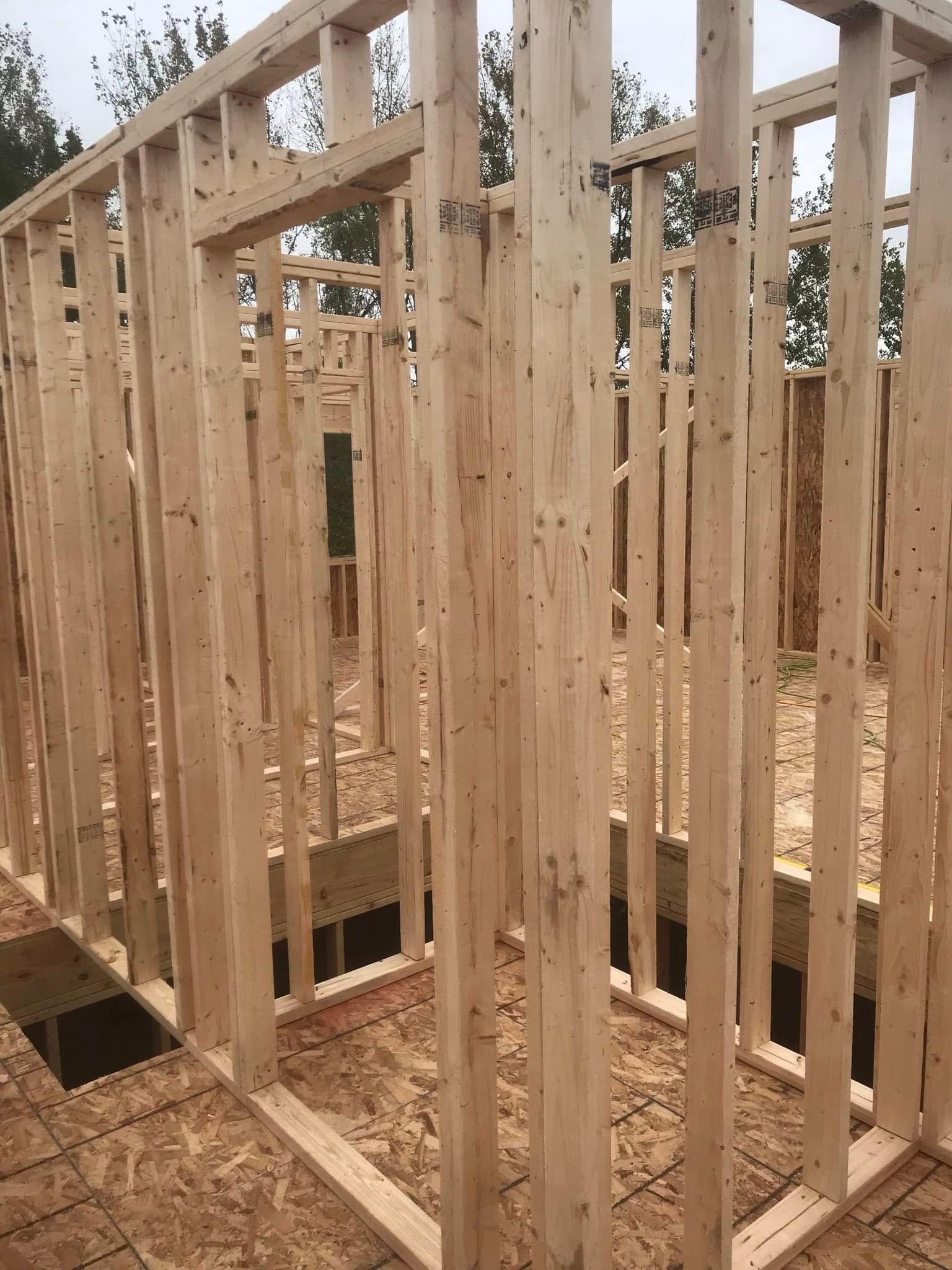 Framed wooden walls of a house under construction, with exposed studs and plywood flooring.
