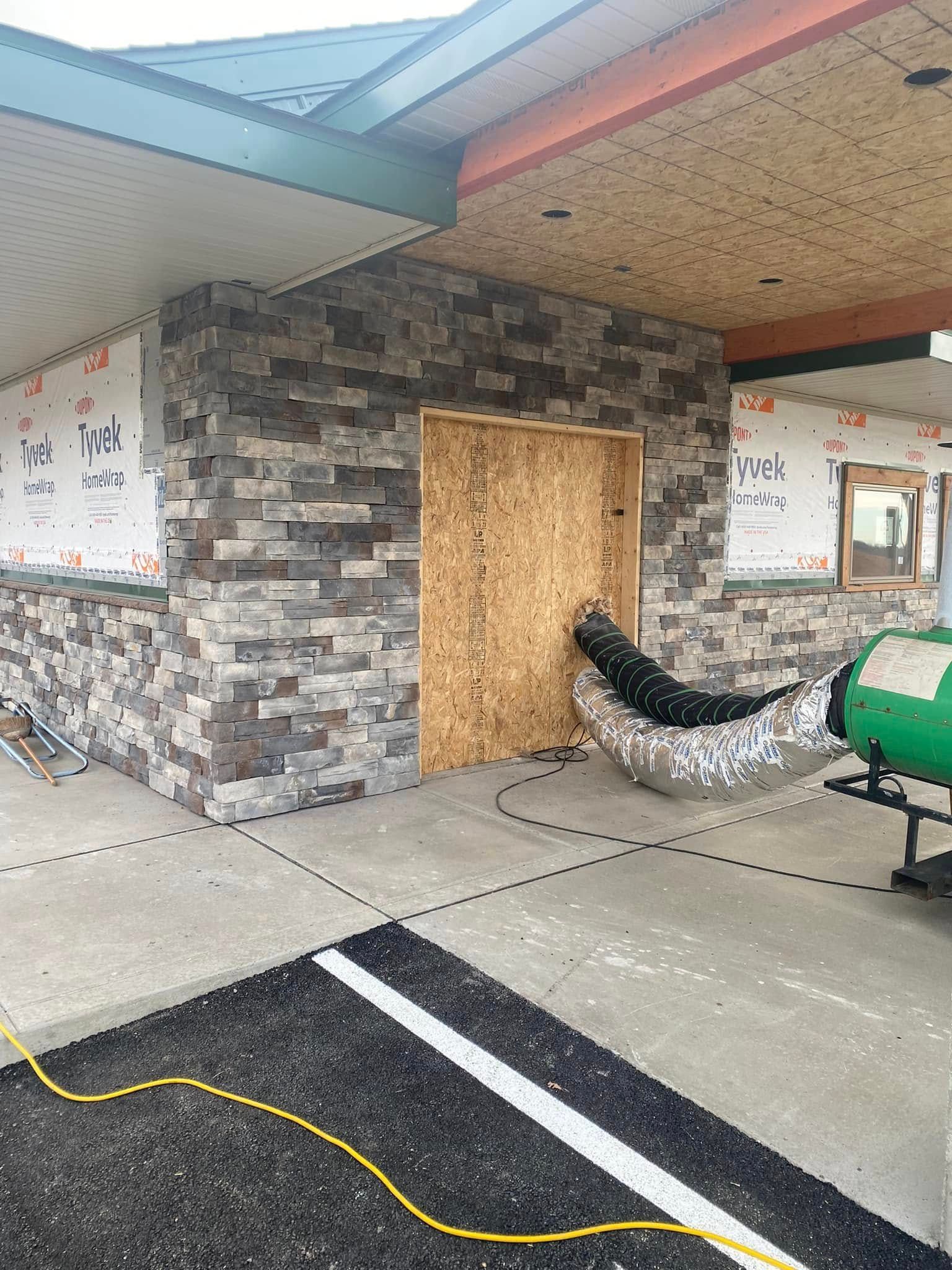 Boarded-up entrance of a building with stone walls and a green construction machine nearby