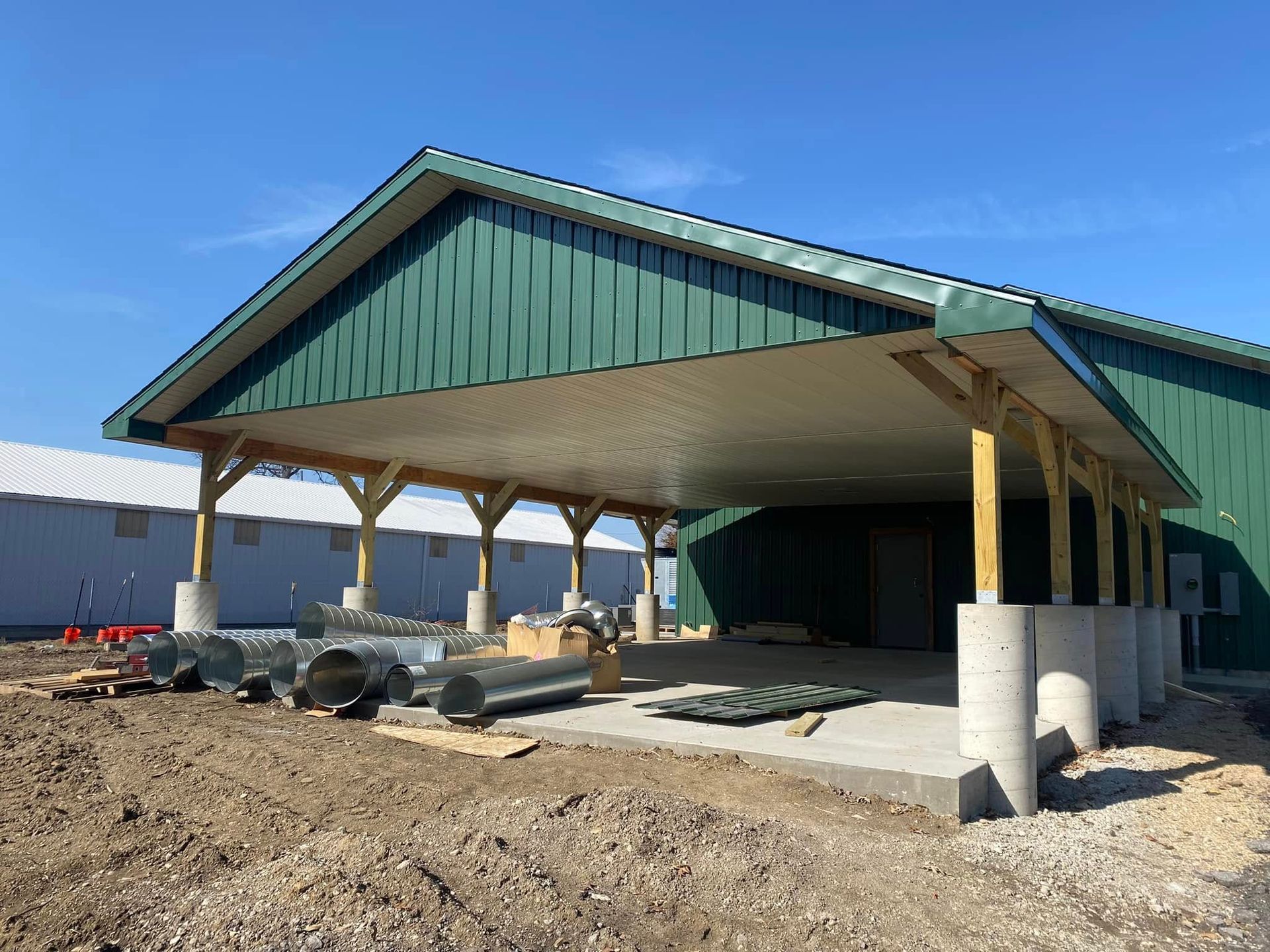 Unfinished green-roofed building under construction with exposed concrete supports and dirt foreground