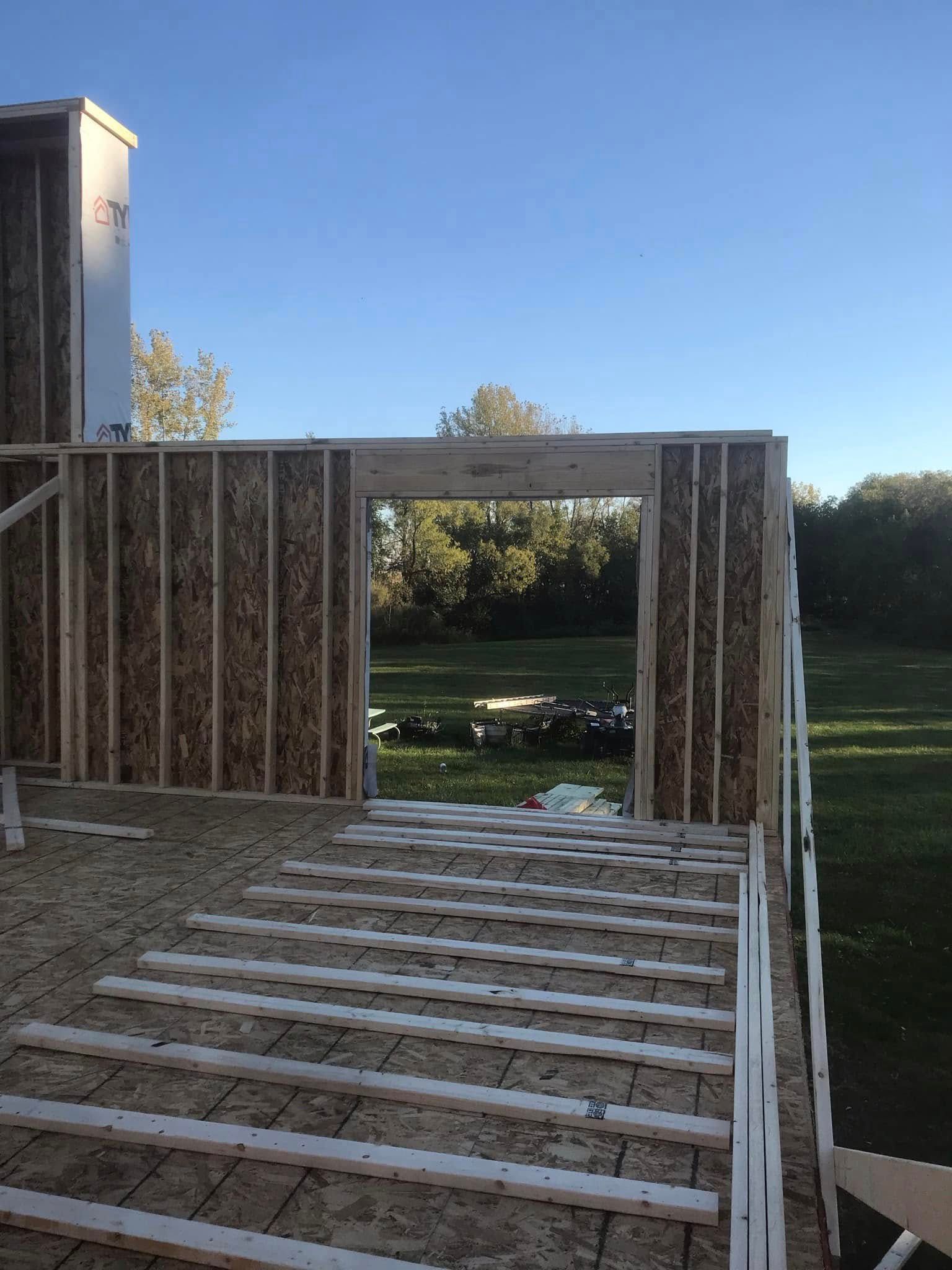 Partially built wooden deck frame beside a house, overlooking a grassy yard and trees. Partially built wooden deck frame beside a house, overlooking a grassy yard and trees.