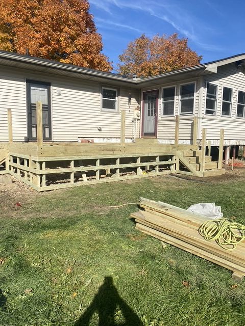 Backyard wooden deck with railing and steps beside a light gray house under a blue sky Backyard wooden deck with railing and steps beside a light gray house under a blue sky