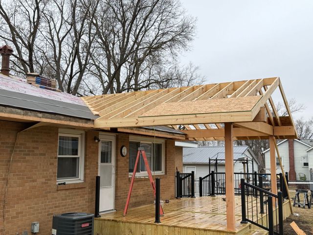 New porch roof under construction on a brick house, with exposed rafters and a red ladder.