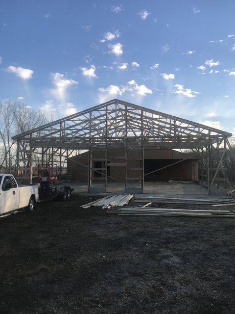 Partially built porch roof under construction with exposed rafters, ladders, and support posts beside a house Partially built porch roof under construction with exposed rafters, ladders, and support posts beside a house