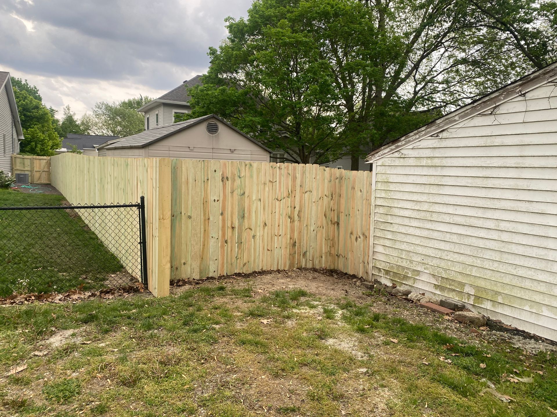 Backyard corner with a newly built wooden fence between two white sheds and a grassy yard