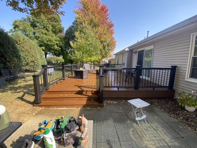 Brown wooden deck platform beside a house, with steps leading down to a brick patio and lawn.