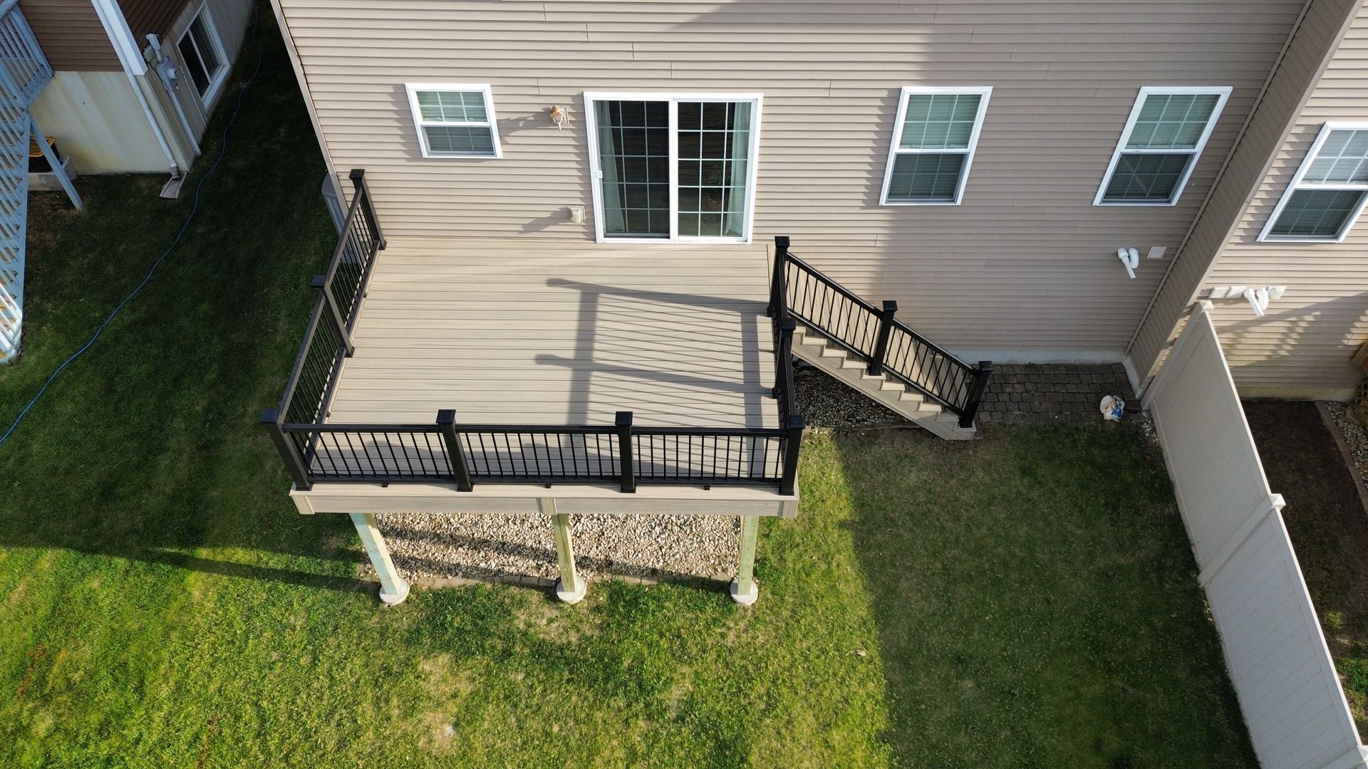 Backyard concrete patio with wooden deck steps beside a white house under a blue sky Backyard concrete patio with wooden deck steps beside a white house under a blue sky