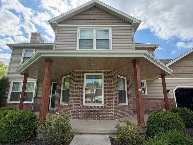 Brick-and-siding two-story house with covered front porch and shrubs in front