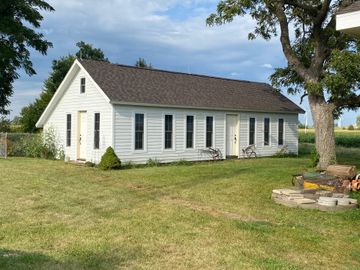 White house exterior with sloped roof, metal ladder, and gravel path beside a grassy yard. White house exterior with sloped roof, metal ladder, and gravel path beside a grassy yard.