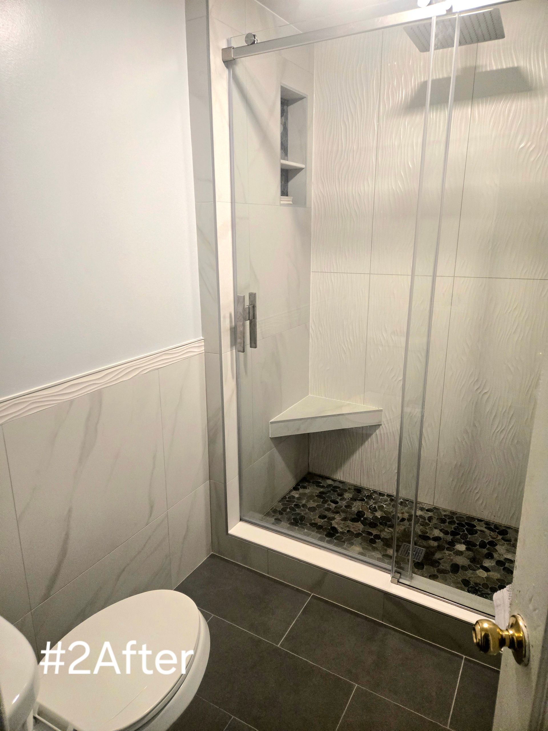 Modern bathroom with white and gray tiles, glass shower door, and pebble shower floor.