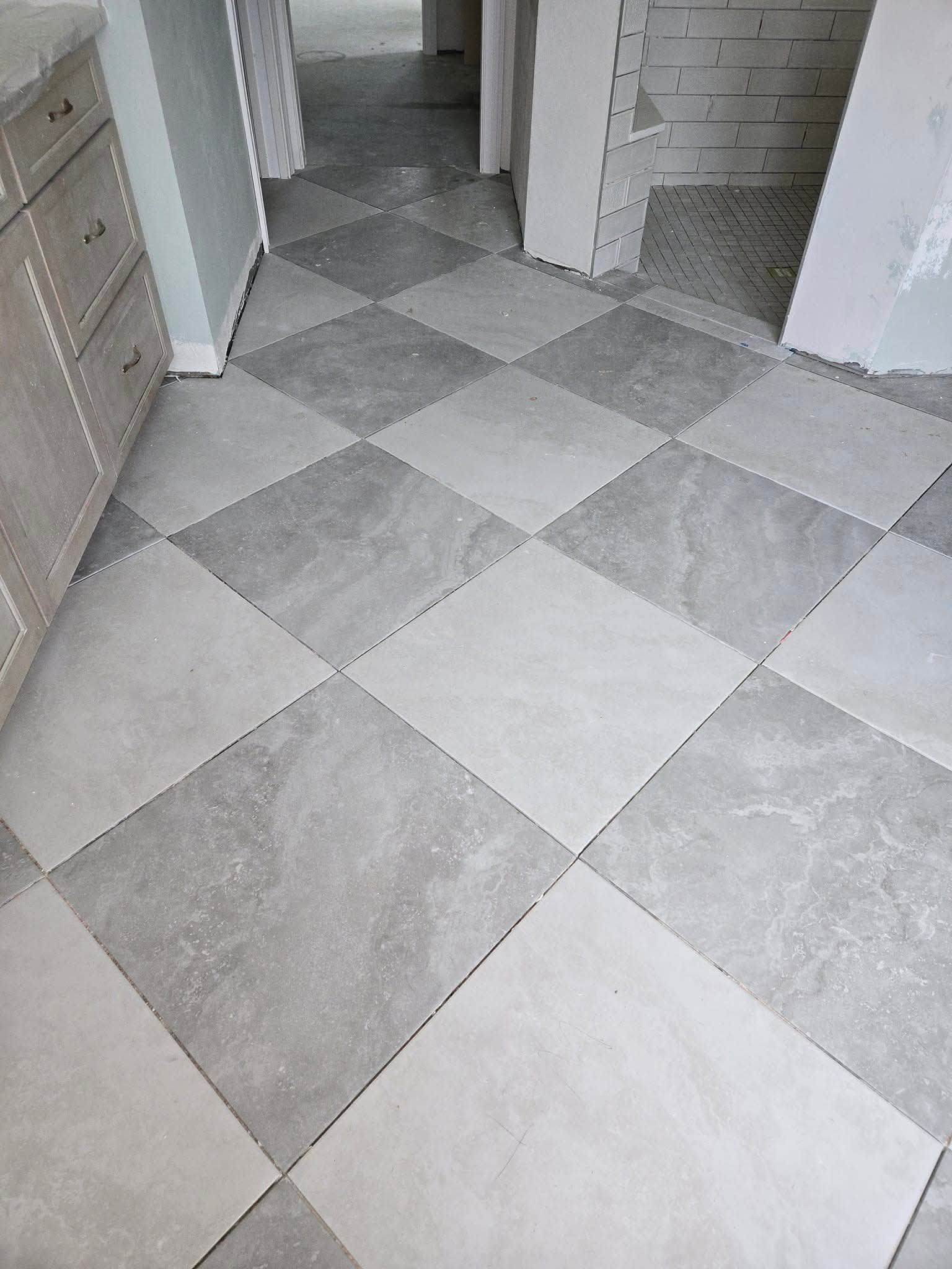 Gray and light gray square tile floor laid in a checkerboard pattern in a room under construction.