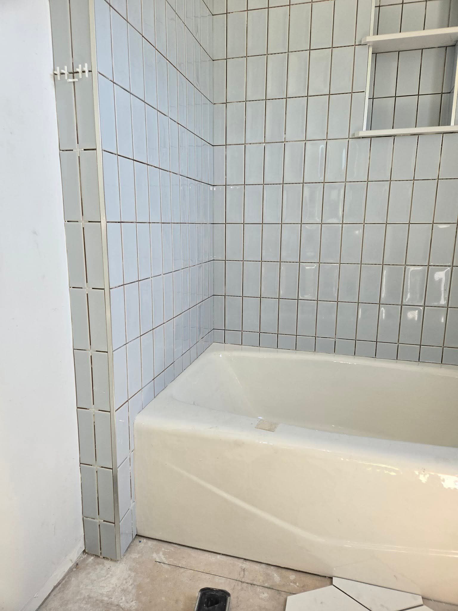 Bathroom corner with light blue textured tiles, a white bathtub, and a built-in shelf.