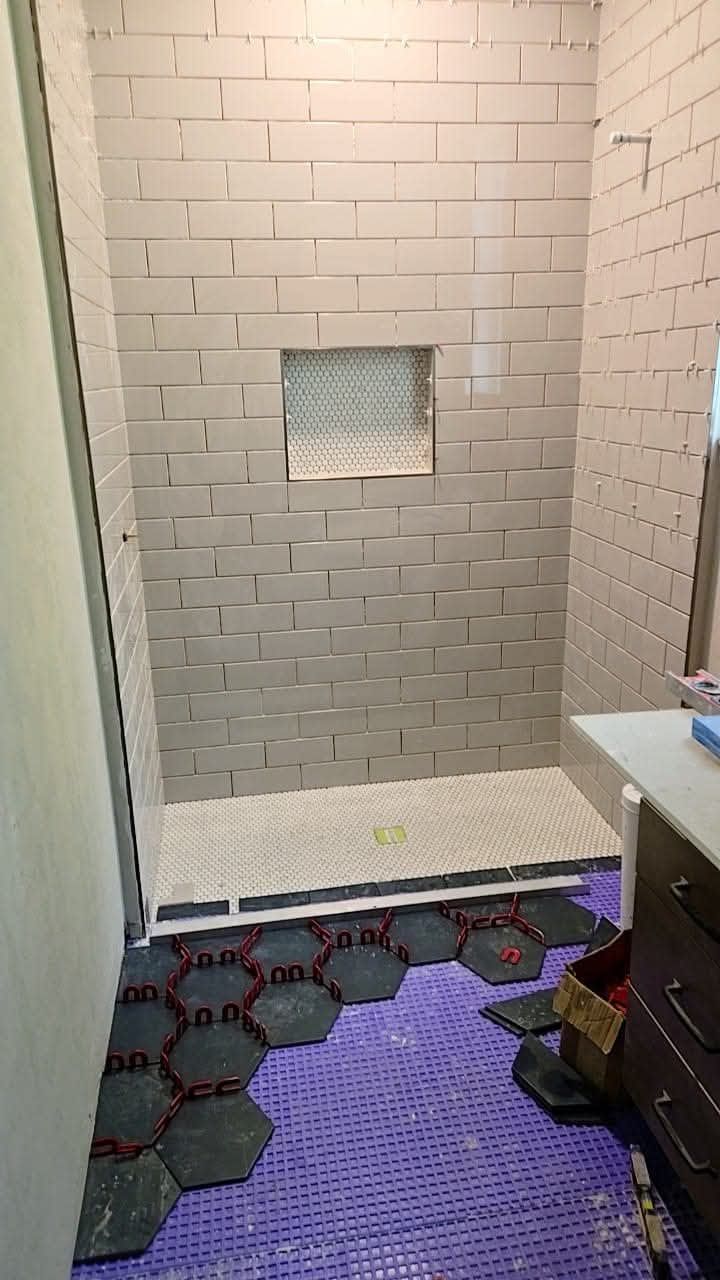 Shower stall under construction, with gray subway tile on the walls and hexagonal tile on the floor