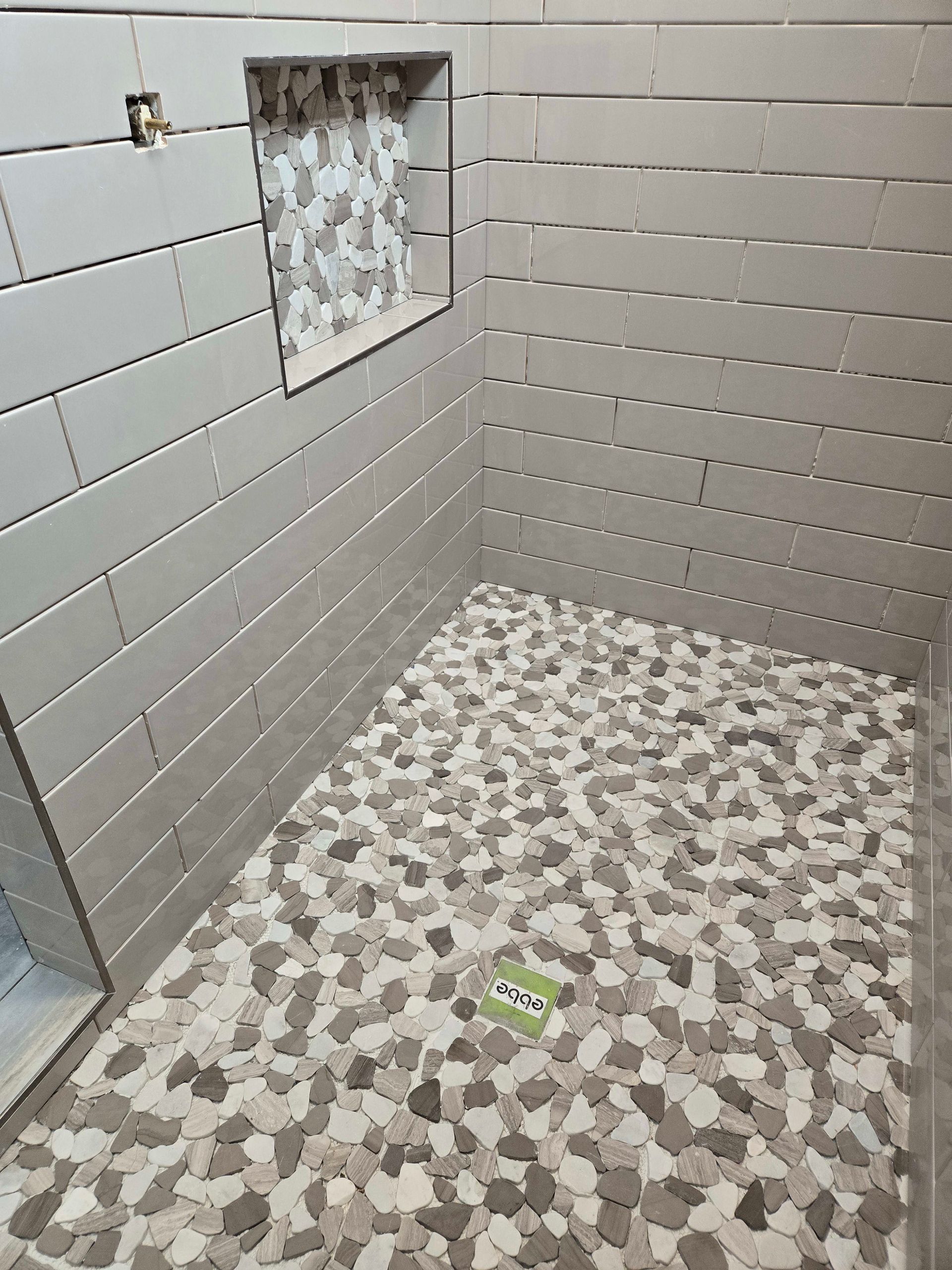 Tiled shower with pebble floor and built-in shelf. Gray, white, and brown tiles.