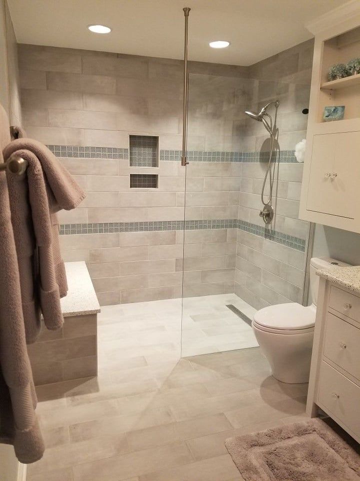 Modern bathroom with walk-in shower, built-in bench, toilet, and vanity. Gray tile and glass enclosure.