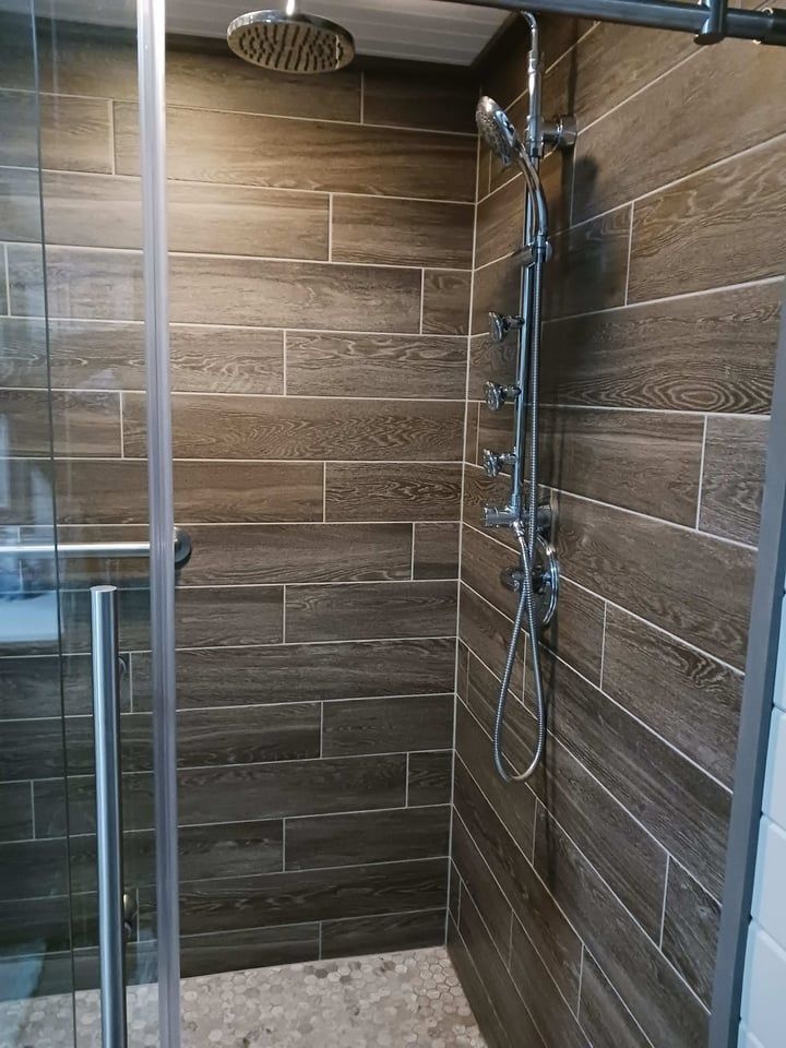 Shower with brown wood-look tile, glass door, and multiple showerheads.