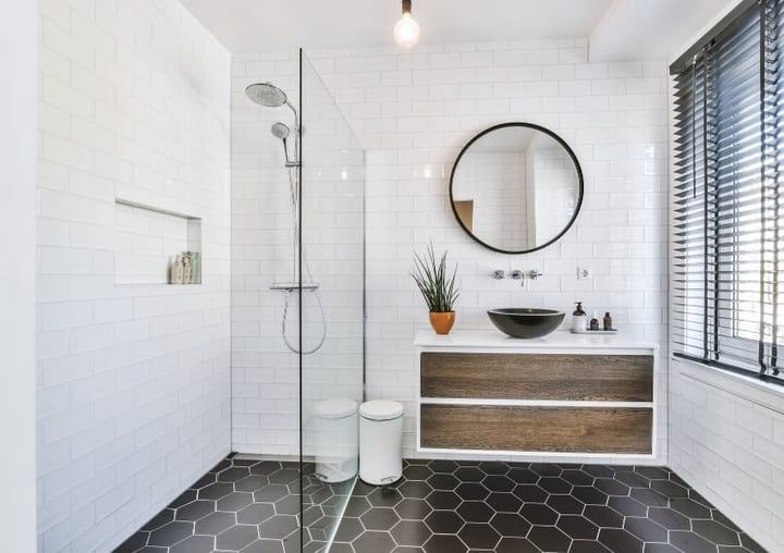Modern bathroom with white subway tiles, hexagonal black floor, glass shower, and wooden vanity.