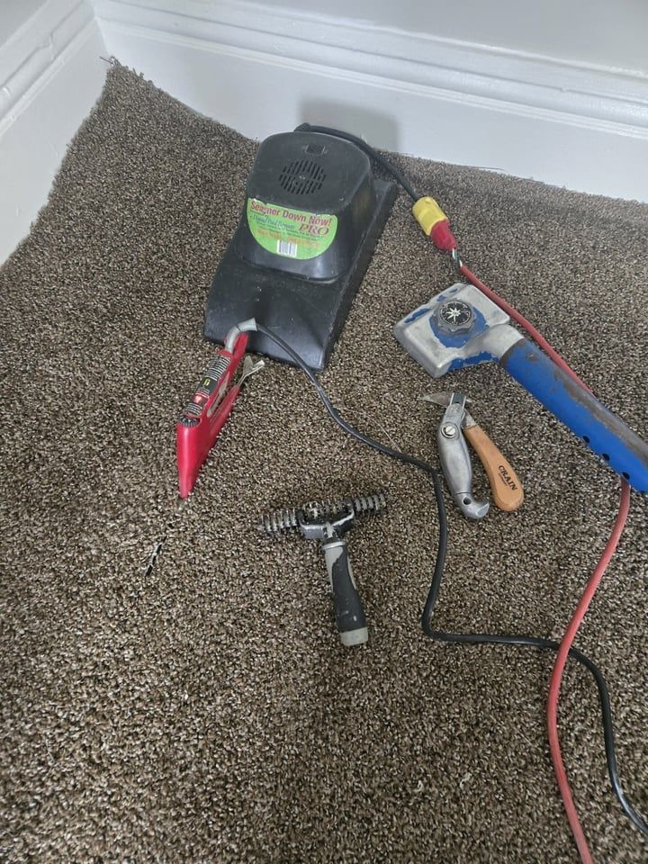 Carpet installation tools on a brown carpet: a power stretcher, knee kicker, knife, and pliers.
