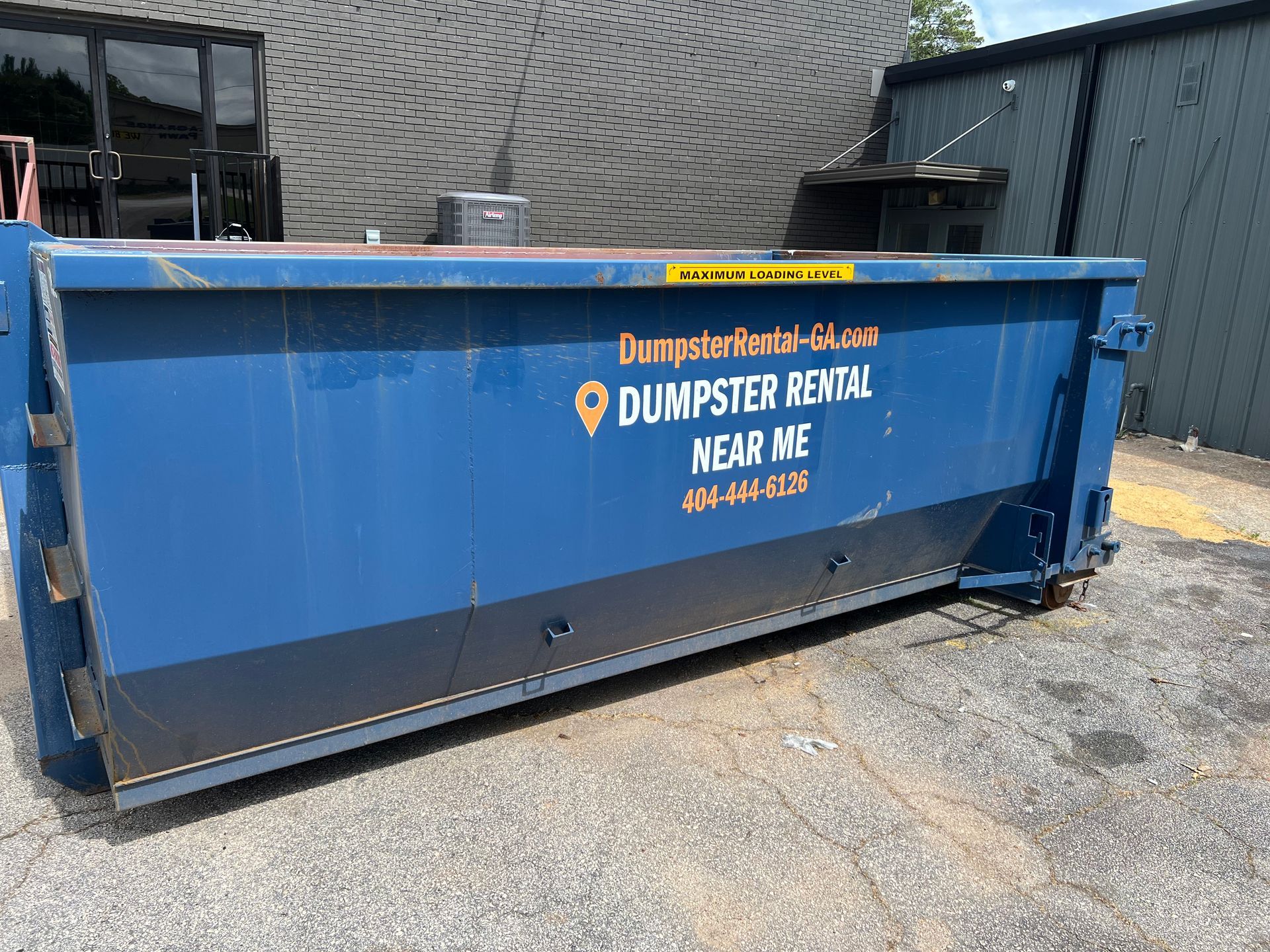 Blue dumpster filled with trash and debris beside a brick building