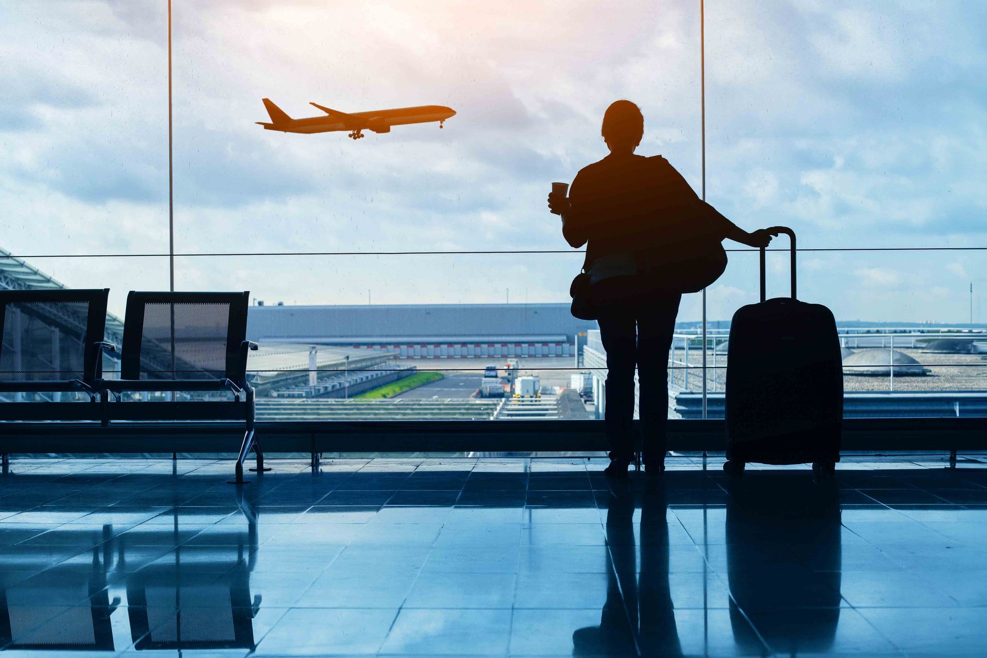 Silhouette of a person at an airport, looking at a plane taking off, with luggage.