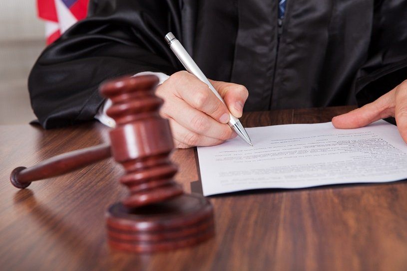 Judge writing on document at desk, gavel in foreground.