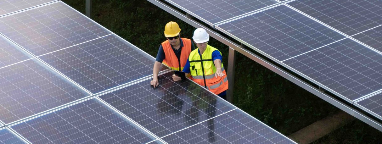 Two workers in safety vests inspect solar panels at a solar farm.