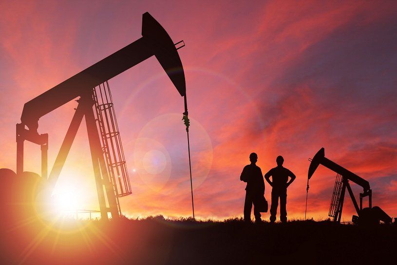 Oil derricks silhouetted against a sunset, with two figures standing nearby.