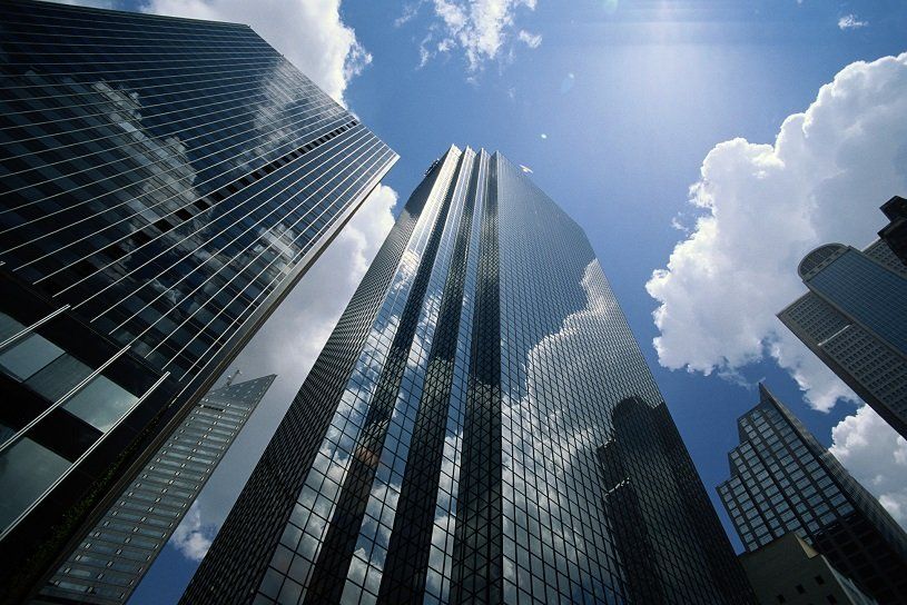 Skyscrapers with reflective glass facades against a bright blue sky with scattered clouds.
