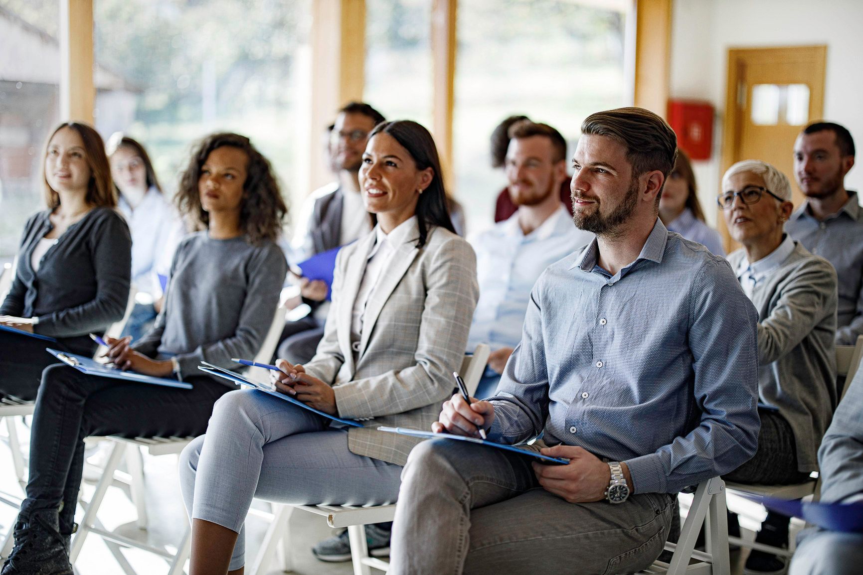 Audience seated in a bright conference room, listening attentively during a presentation