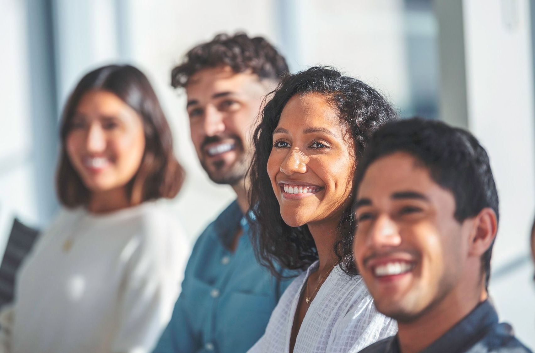 Group of smiling people in a bright office space, looking to the side.