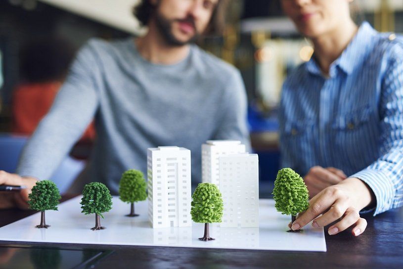 Two people arranging miniature trees around building models on a table.