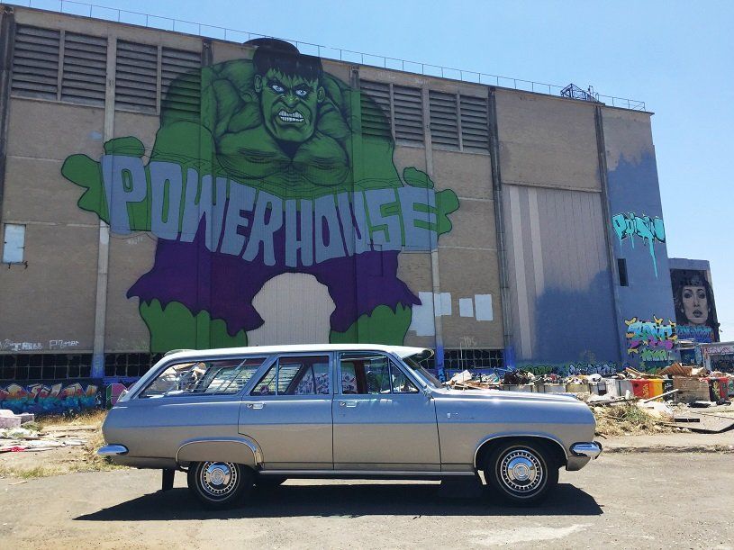 Silver station wagon parked in front of a building with Hulk mural that says 