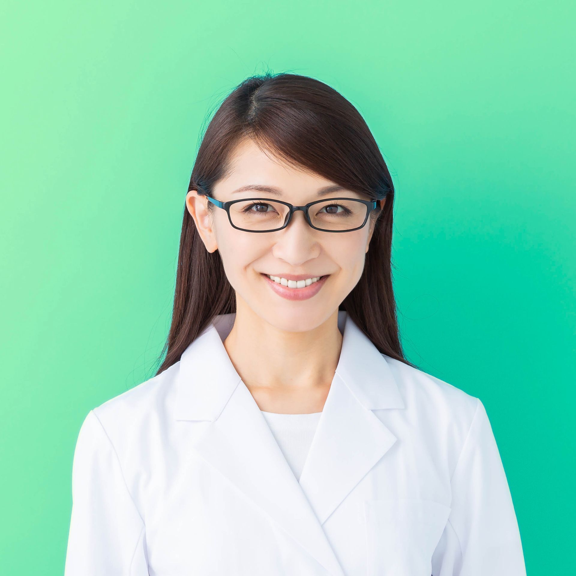 Woman in glasses and white coat smiling, against a green background.