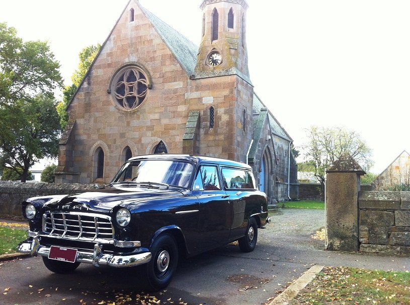 Black vintage station wagon parked in front of a stone church.