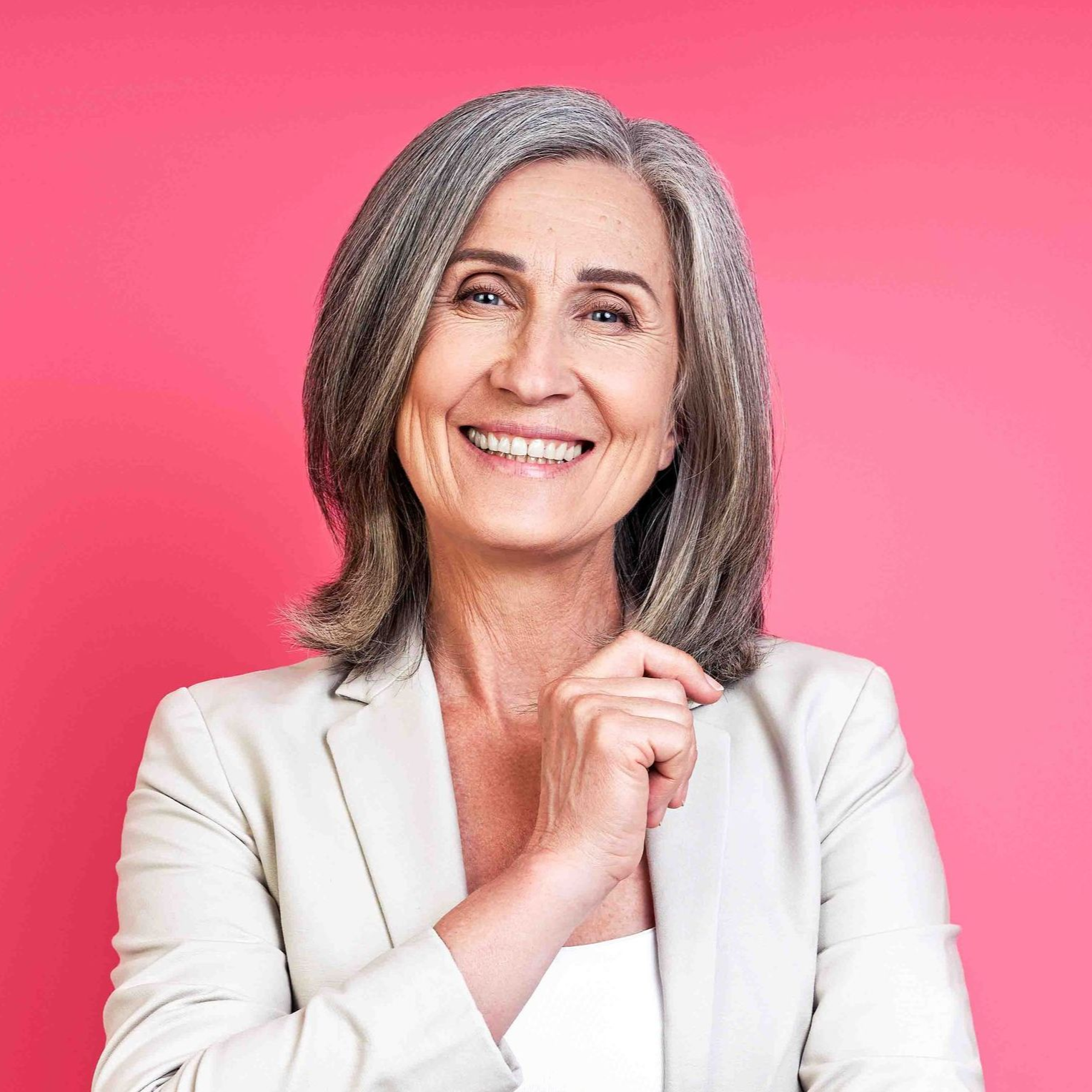 Woman smiling, wearing a white blazer, against a pink background.