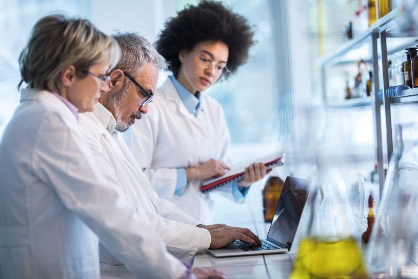 Three lab workers in white coats examining data on a laptop in a lab.
