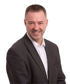 Man in a suit smiles at the camera against a white background.