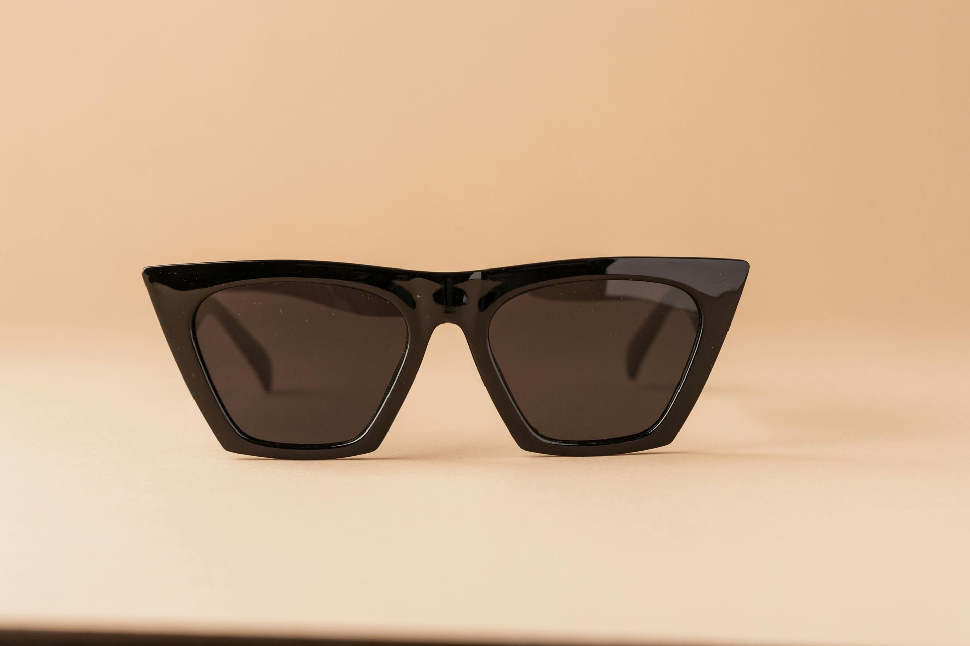 Gafas de sol negras con montura angular sobre una superficie de color bronce claro.