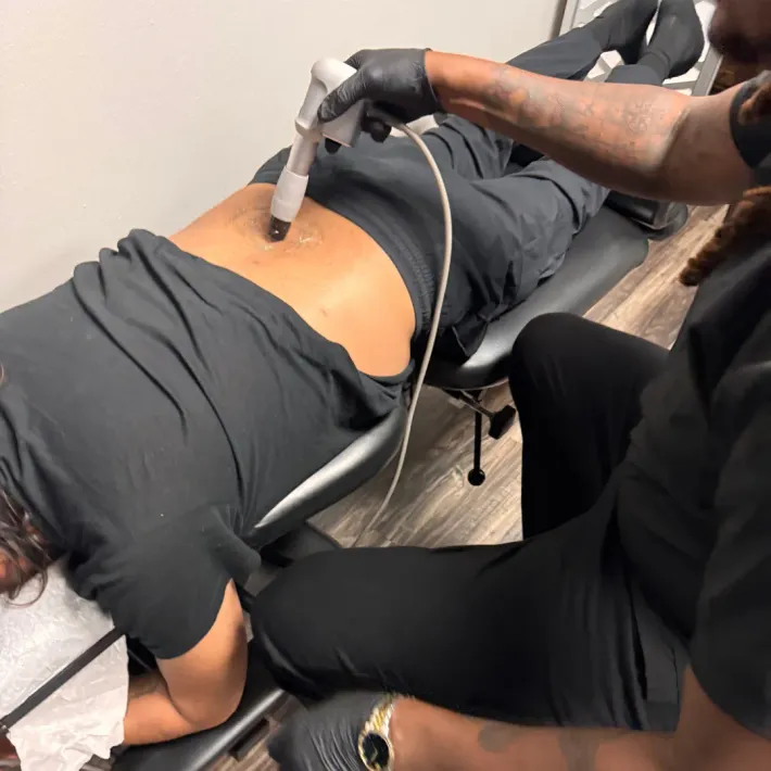 Physical therapy treatment on a patient lying face down, with a handheld device on their lower back.
