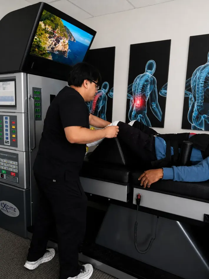 Clinician assisting a patient on a chiropractic table with spine anatomy posters on the wall