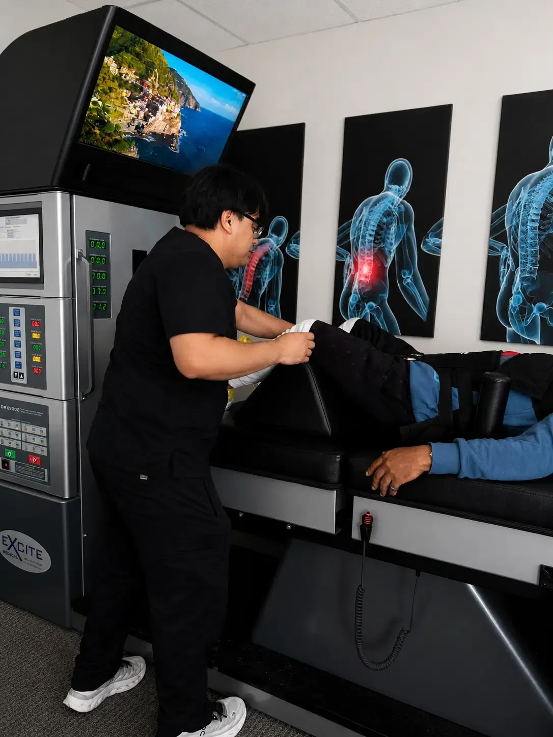 Worker operating a medical imaging scanner on a patient in a clinical room with diagnostic display screens