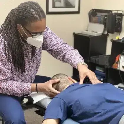 Woman in a mask examining a patient lying face down on an exam table in a clinic office
