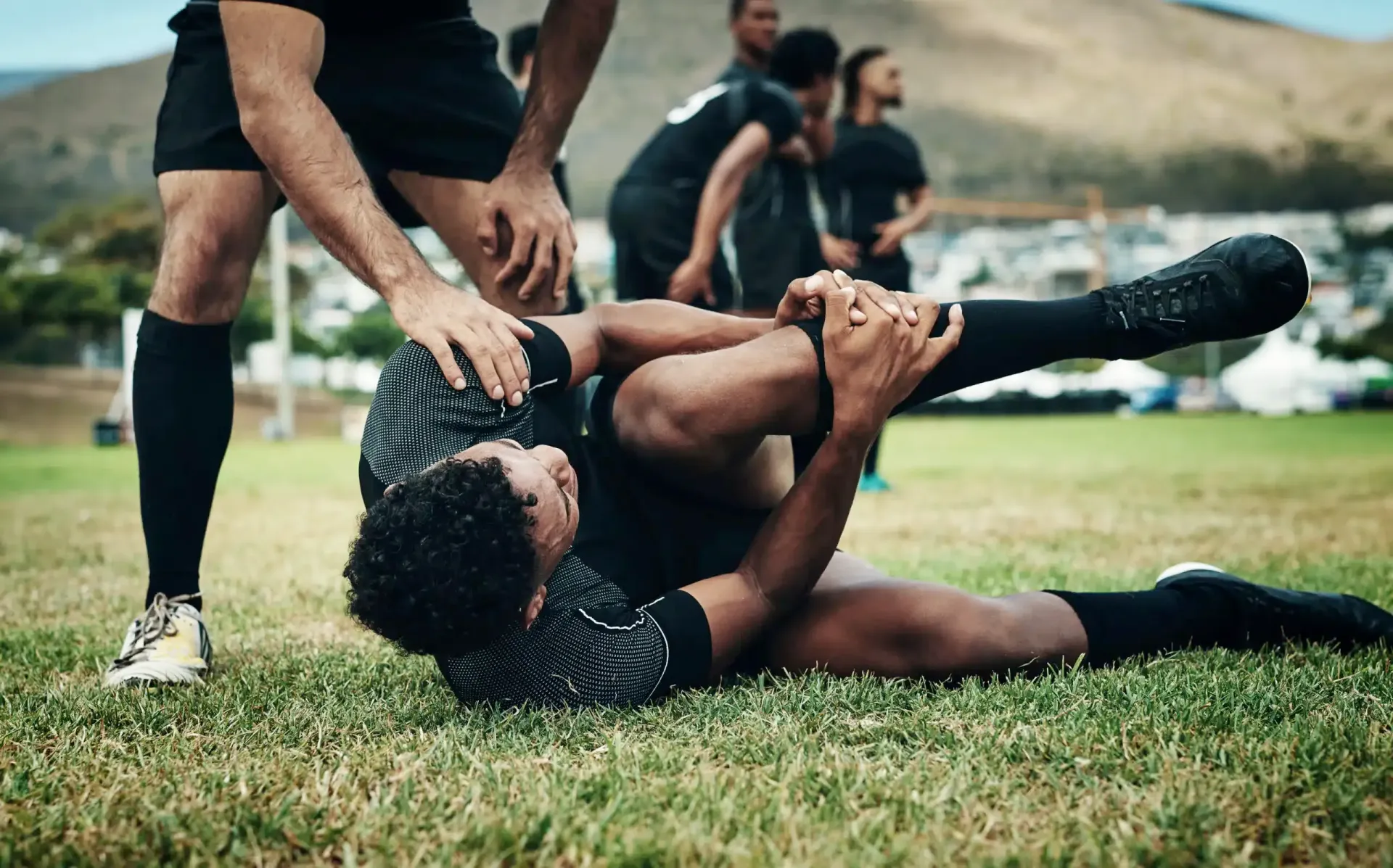 Rugby player tackled on a grassy field, gripping the ball while teammates stand nearby