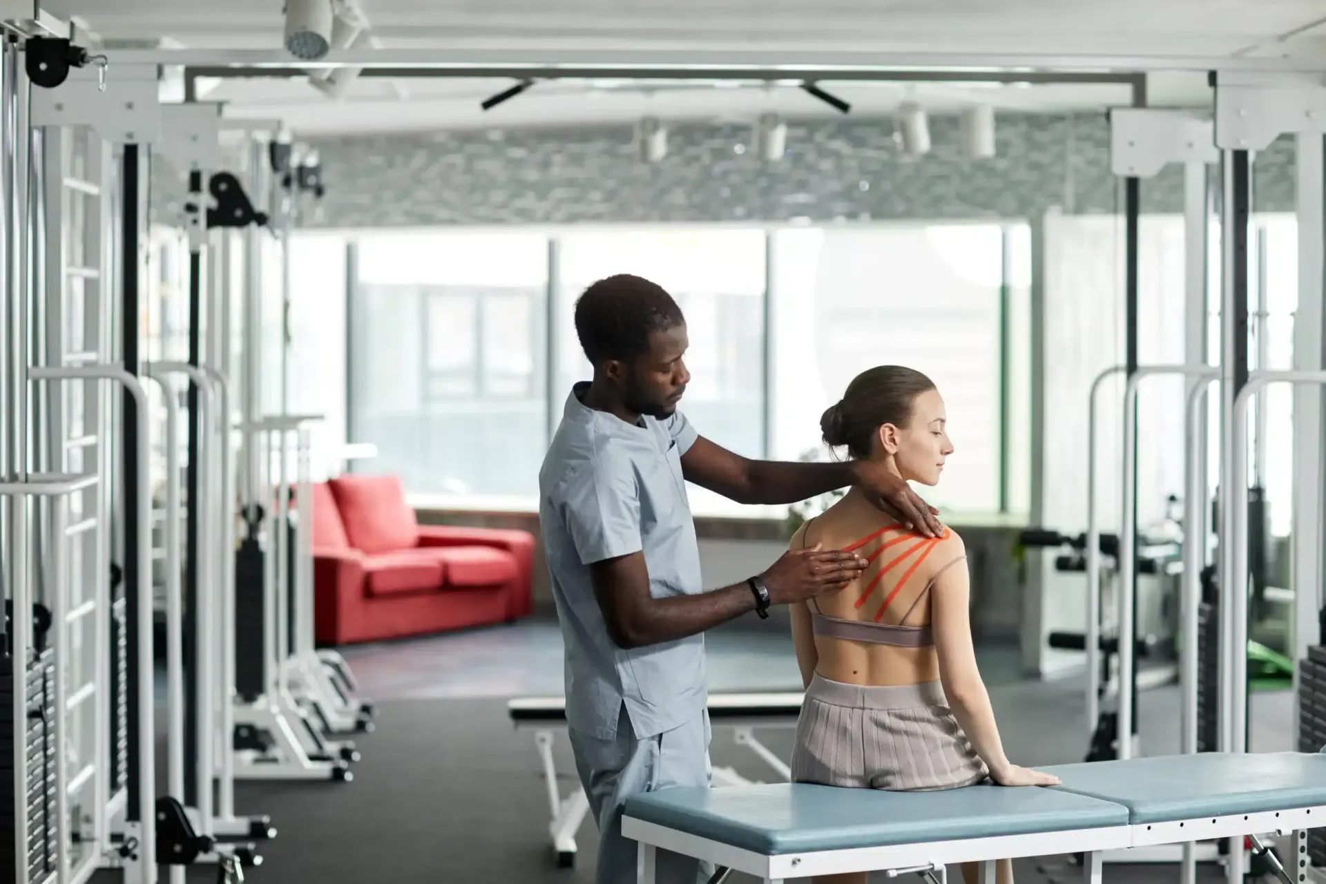 Physical therapist stretching a patient's neck in a bright gym with exercise equipment