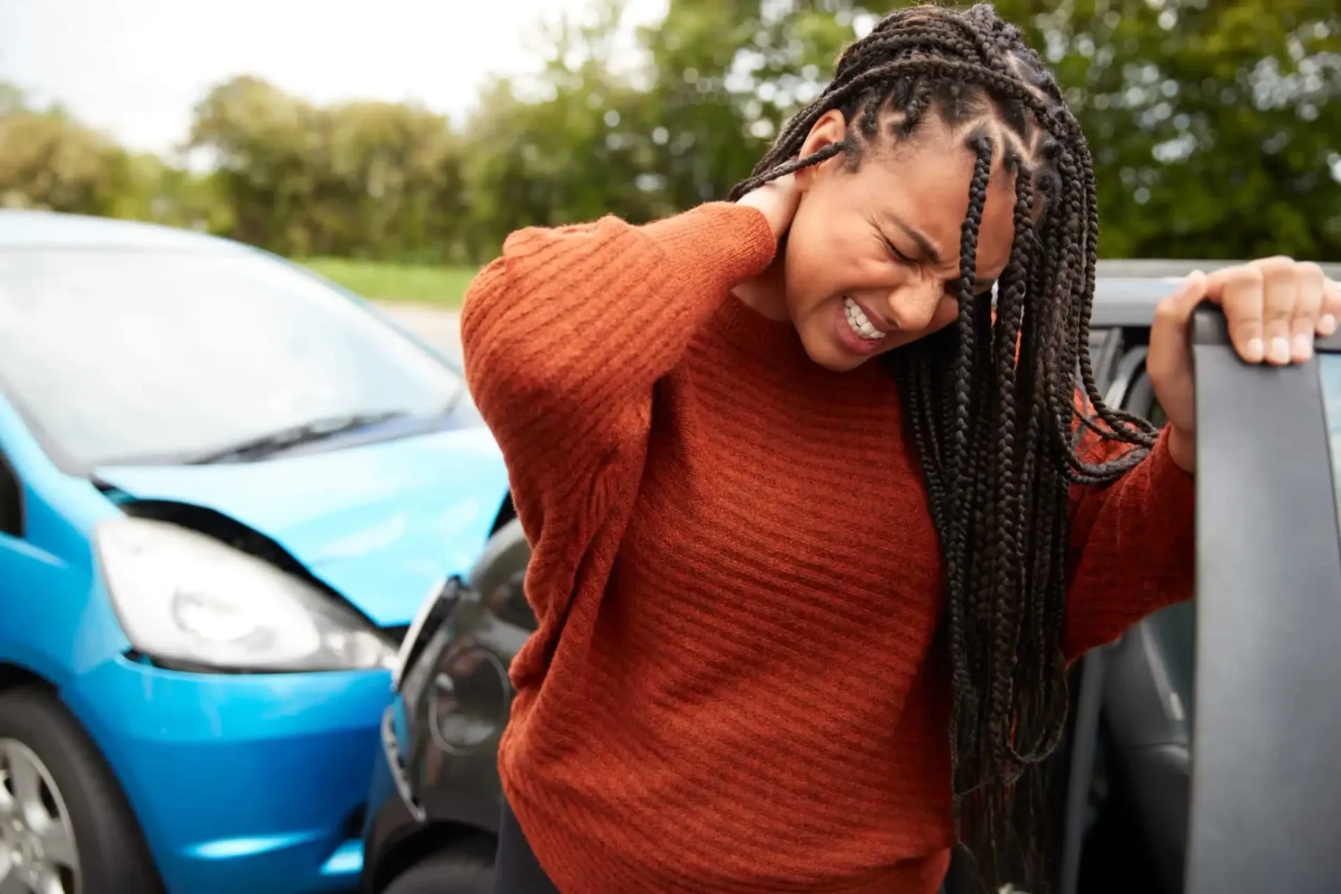 Woman in orange sweater grimacing beside damaged cars after a collision