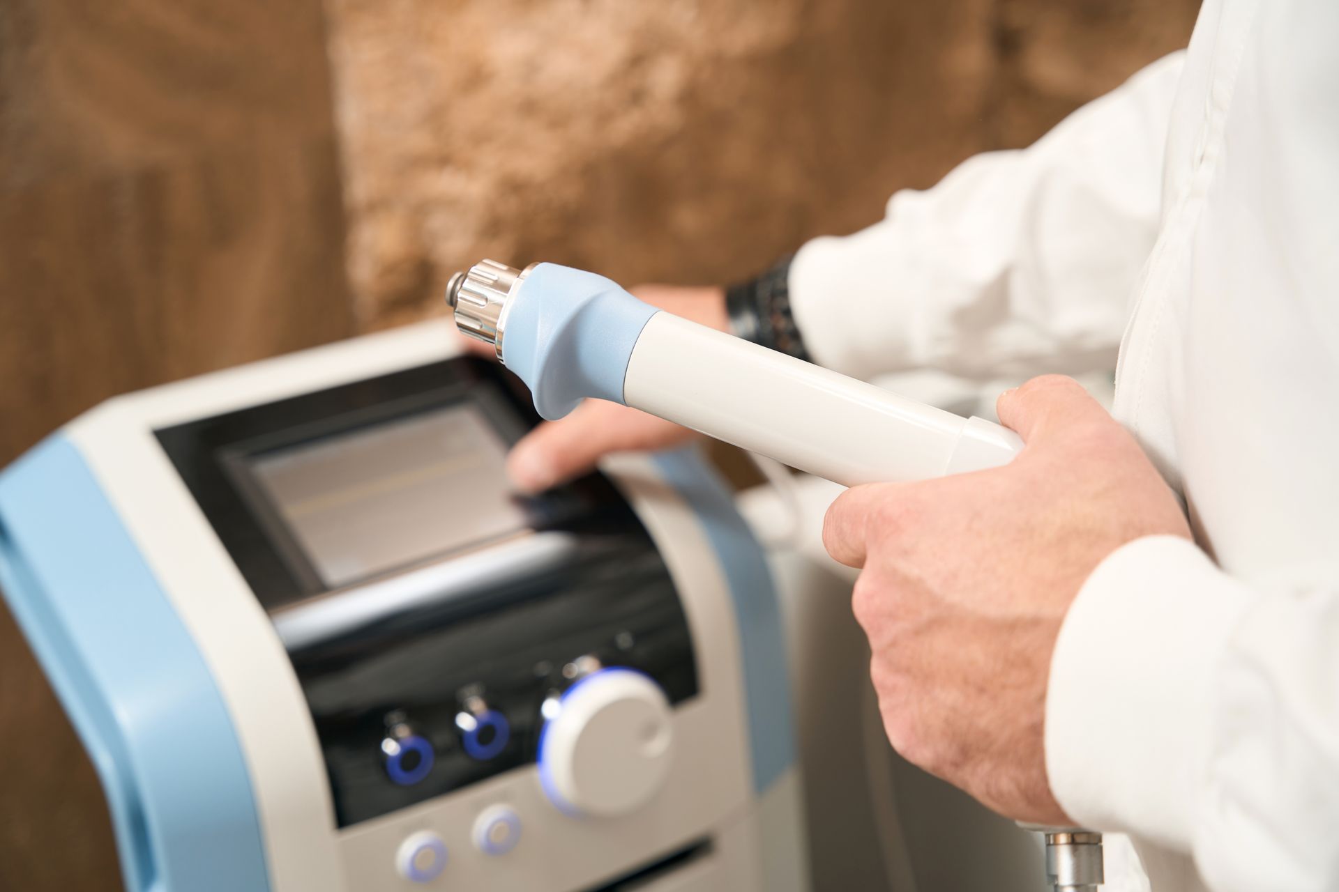Hands holding a blue and white medical device next to a control panel on a clinic machine