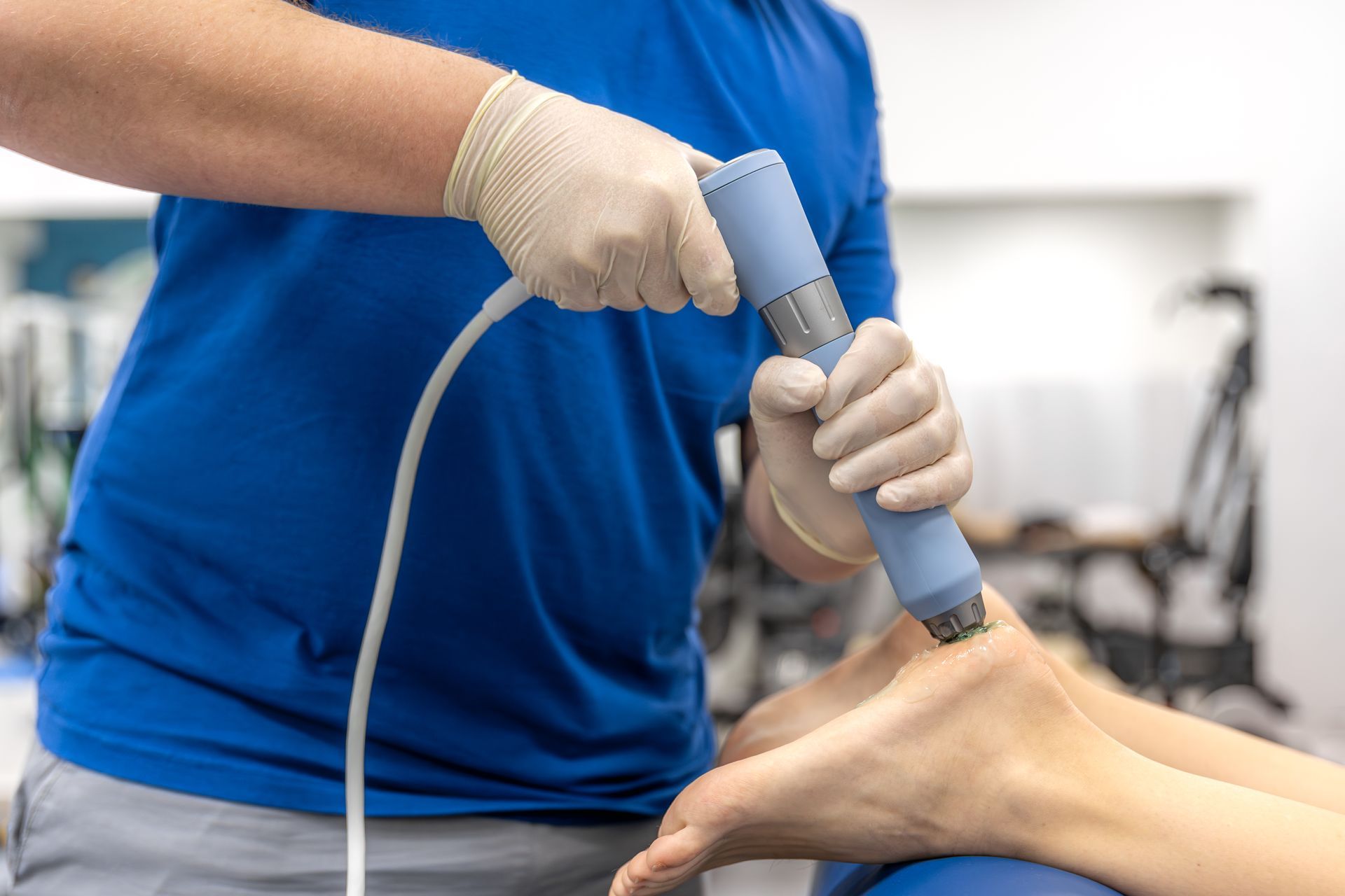 Gloved clinician using a handheld medical device on a patient’s hand in a clinic.