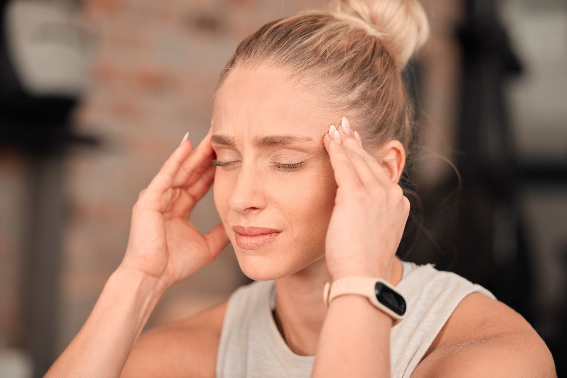 Person holding temples with eyes closed, looking stressed or in pain indoors